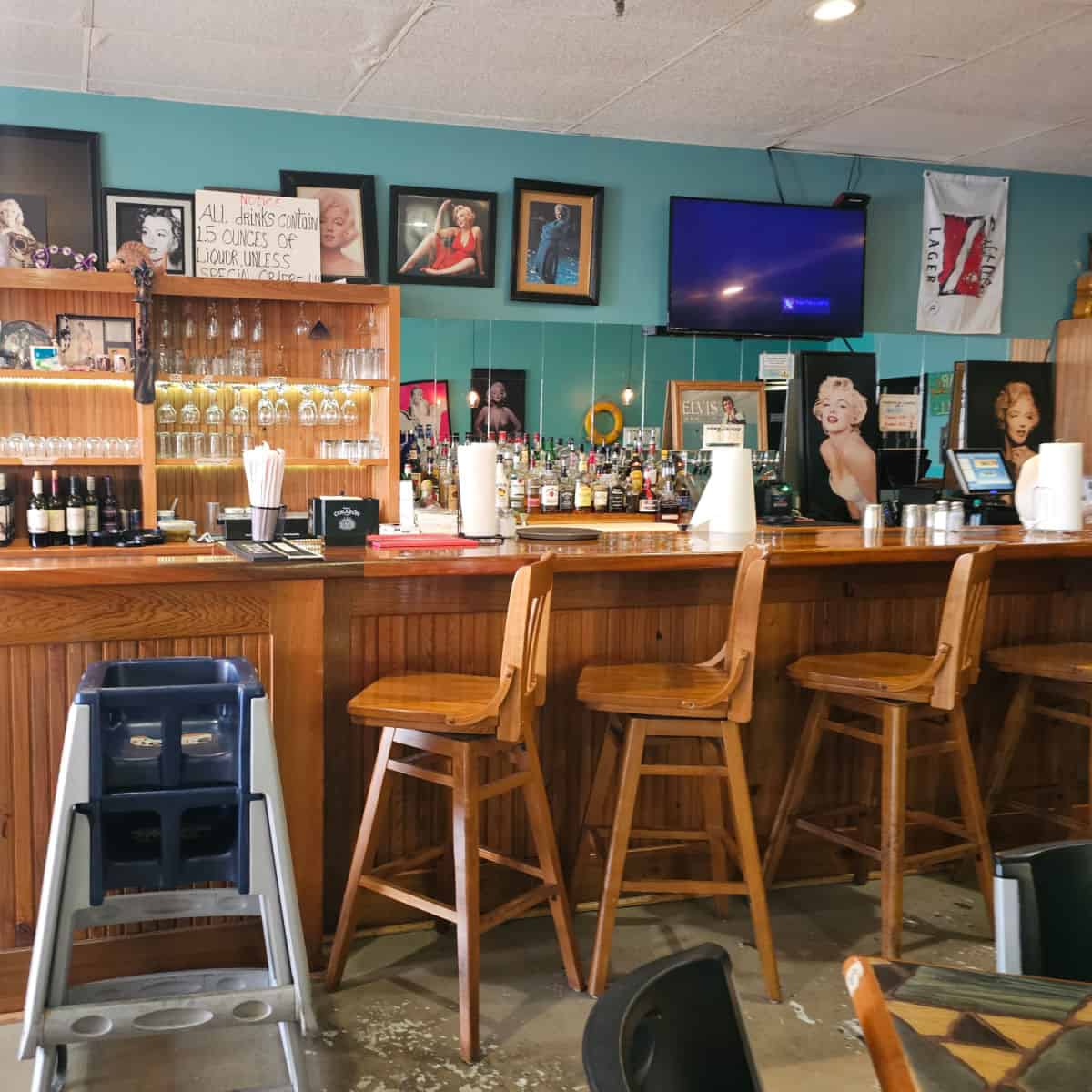 indoor bar with art on the wall, shelves of glases,tall chairs against the bar with a high chair