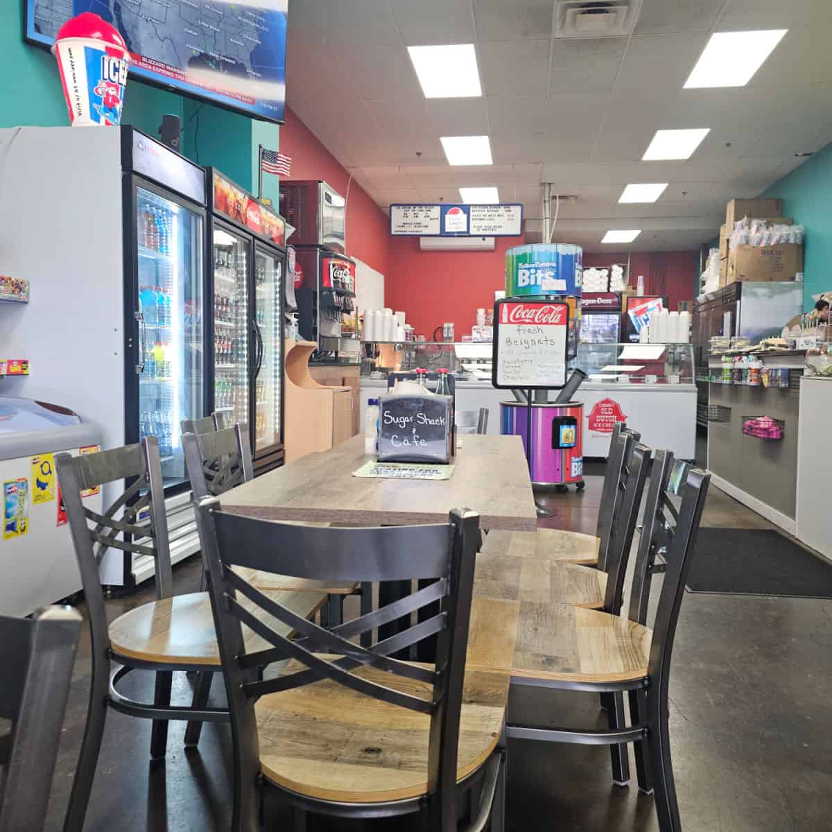indoor seating with tables and chairs, red paint on the wall, drink refrigerator on the left side