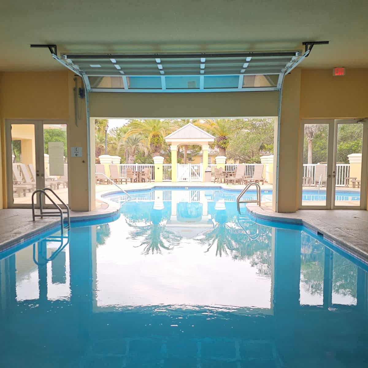 Indoor pool looking towards an outdoor pool with a garage door up in between them