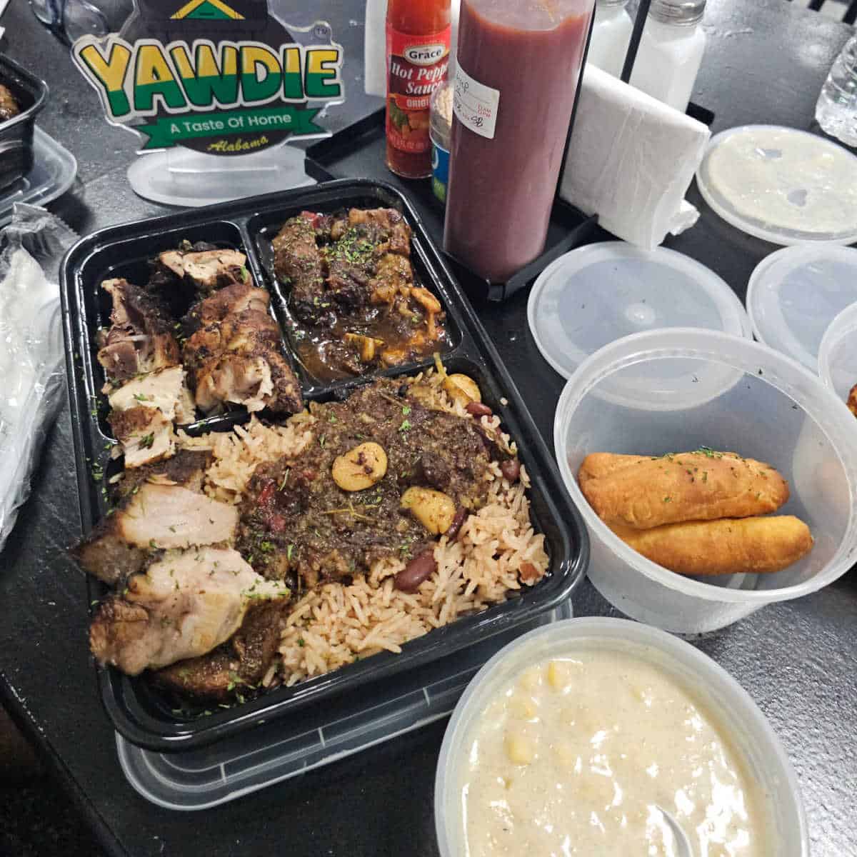 Tray with jerk chicken, oxtails, and rice next to a bowl of porridge and festival bread