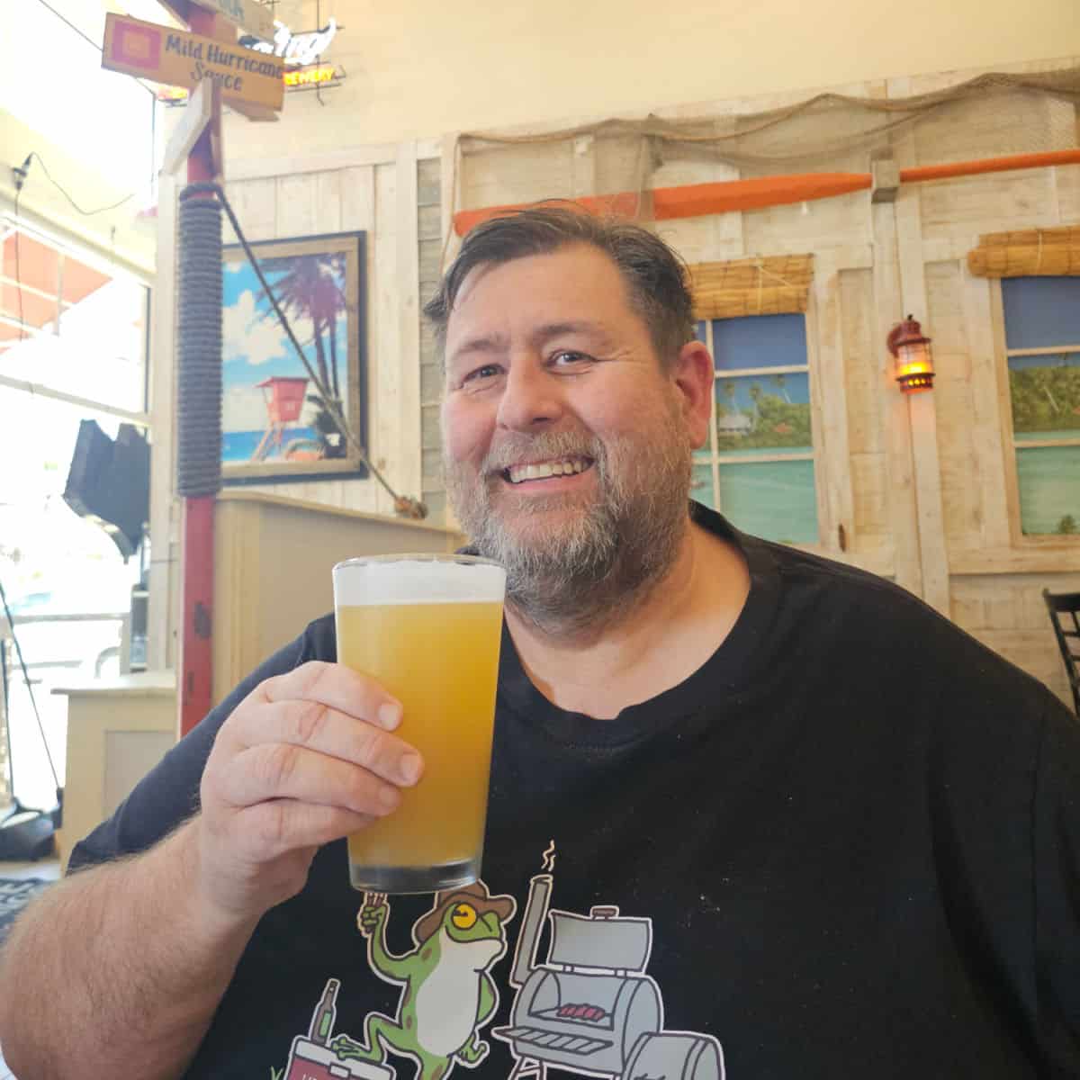 John holding a beer with decorated walls behind him