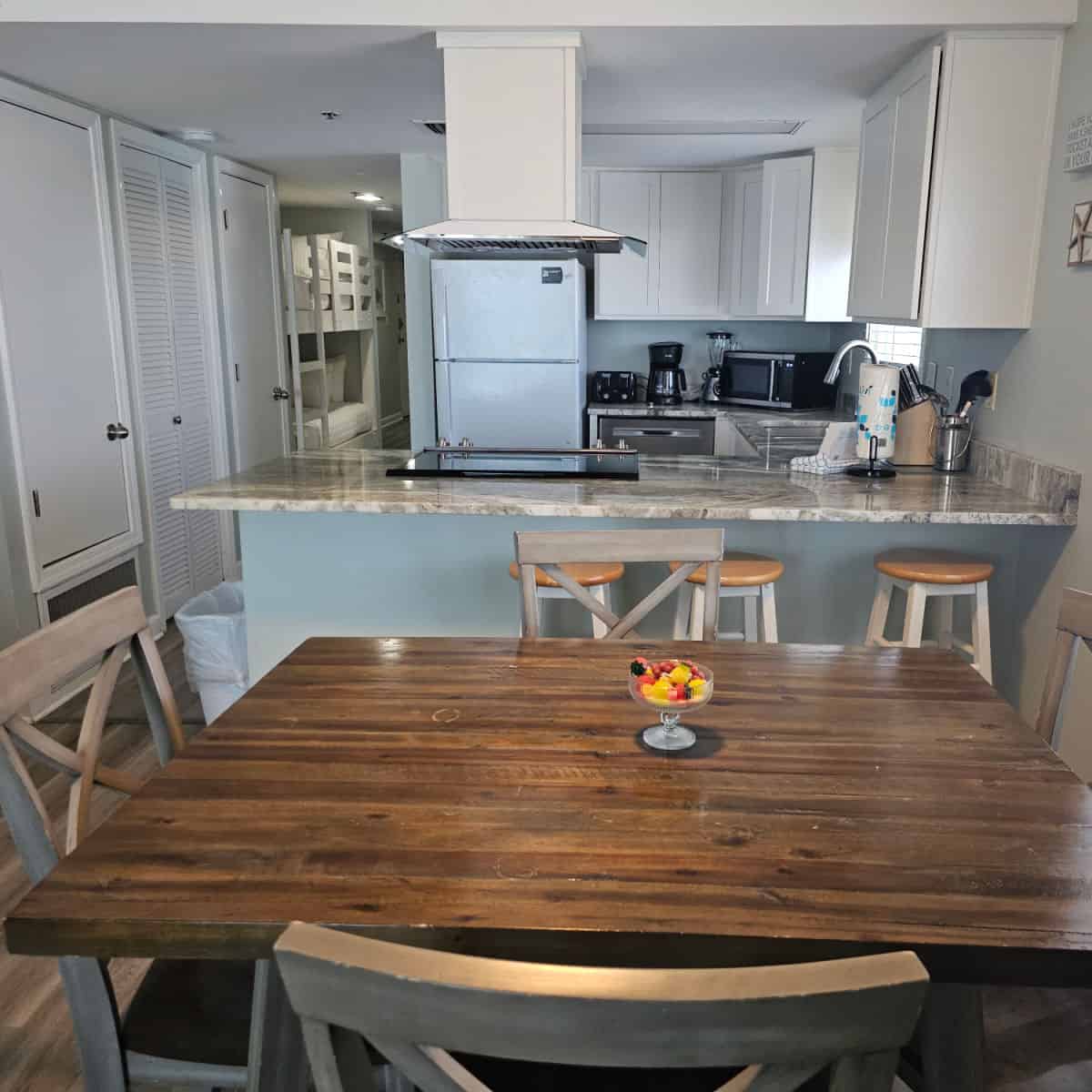 looking over a dining room table with a glass of fruit to a kitchen with white cabinets