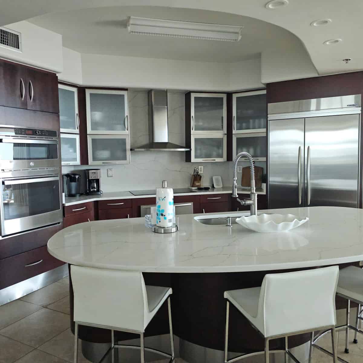 Kitchen area with stainless steel appliances with white chairs at the counter.