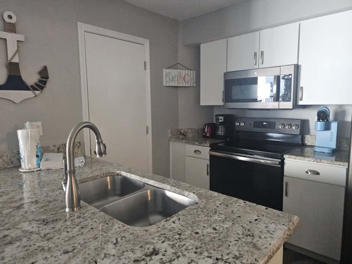 Kitchen with blue Keurig, microwave over an over, white cabinets, sink with paper towels, anchor art on the wall