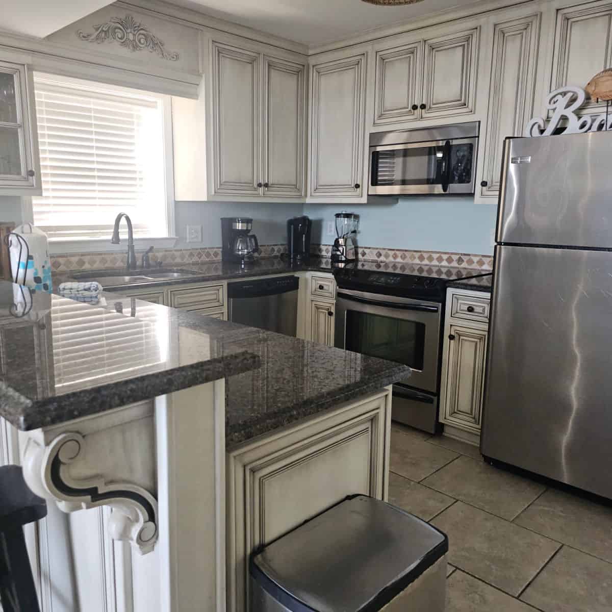 Kitchen area with white antique looking cabinets, stainless steel appliances, cofee maker, blender on the counter