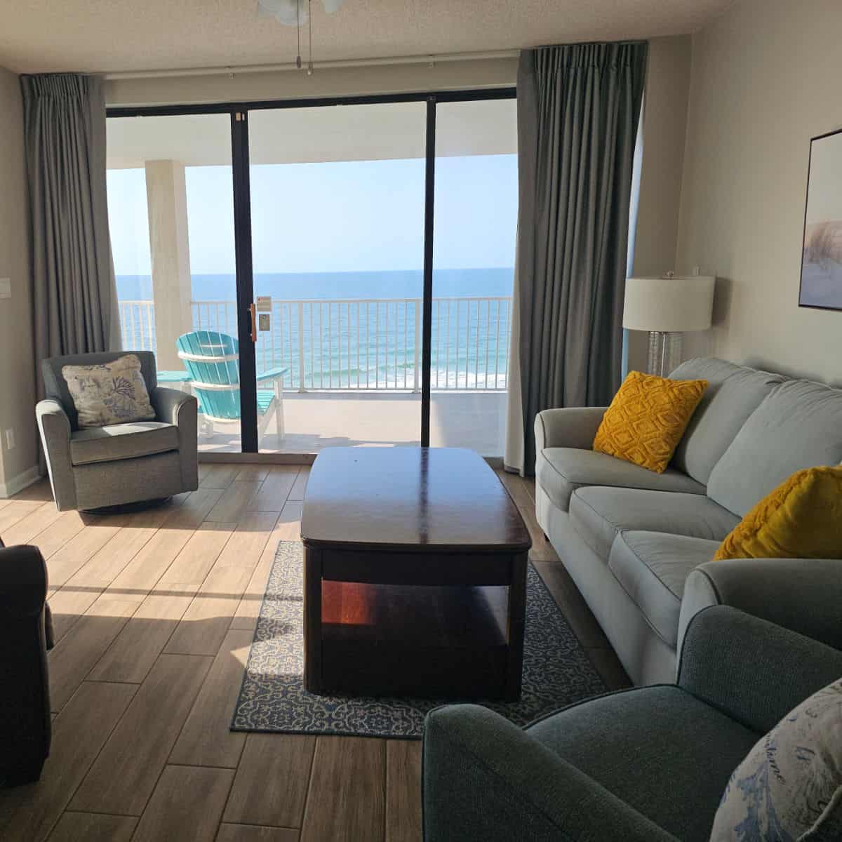 living room with grey couch and chair, adirondack chair on the balcony looking out over the Gulf