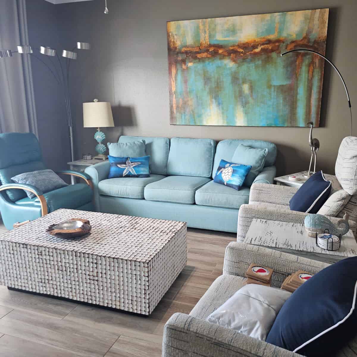 living room with a light blue couch, light blue chair, and grey chairs, coffee table in the middle of the floor, vibrant art on the wall,