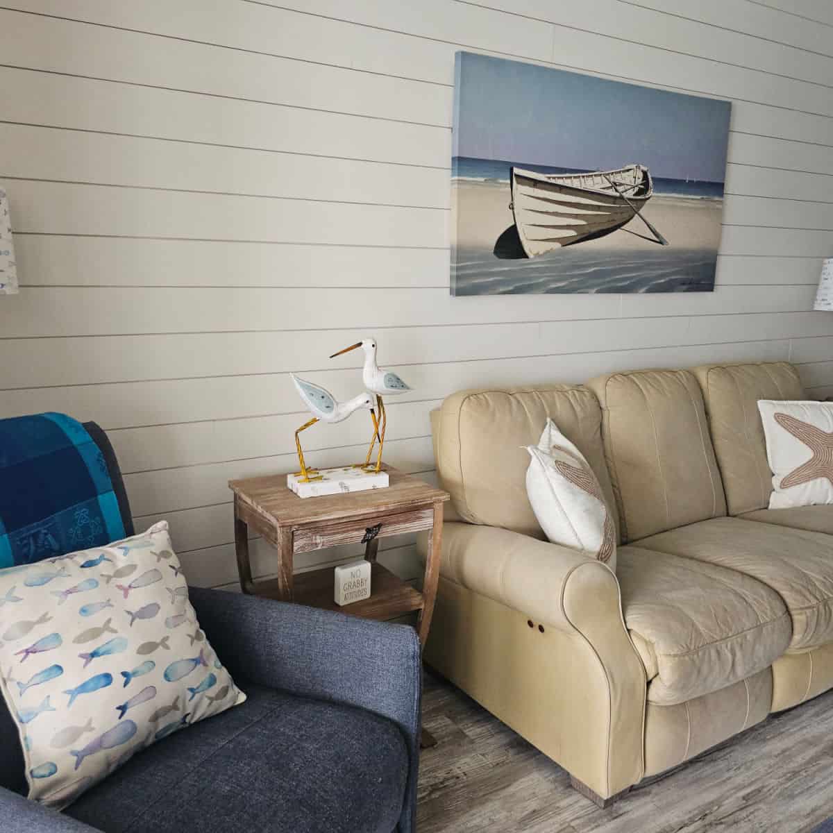 living room area with brown couch, blue chair, bird sculptures on a wooden table, boat art on the wall