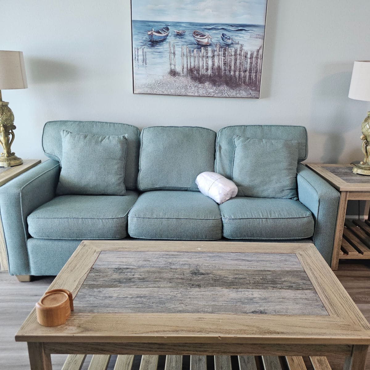 light green couch with a boat art picture over it, lamps on either side, wooden table in front