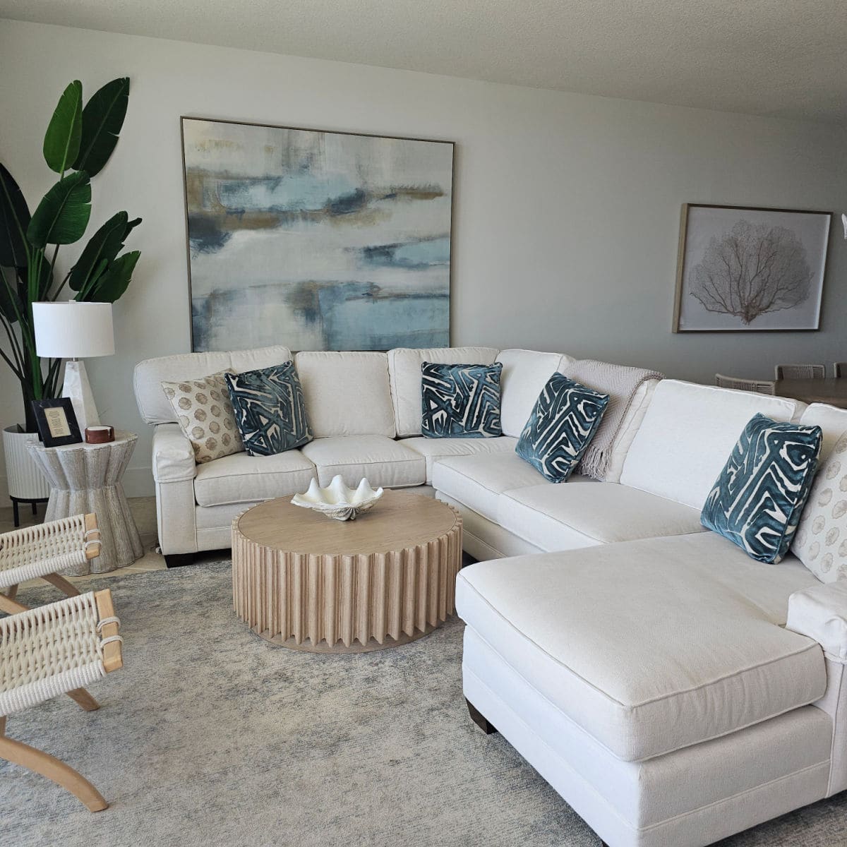 Large white couch with colorful pillows, greenery in the corner, paintings on the wall,
