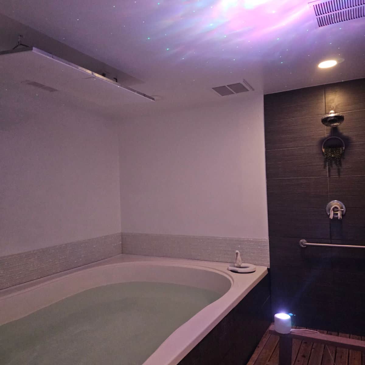large float therapy pool with no cover, next to a shower, and colorful lights on the ceiling