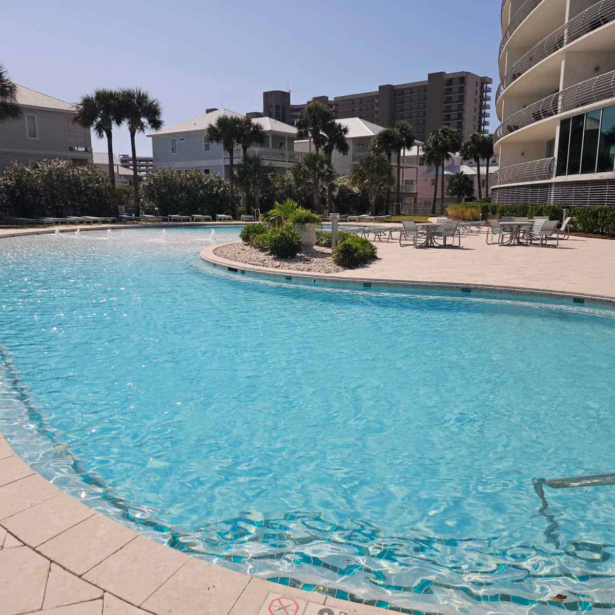 large outoor pool with palm trees in the background along with tables and chairs on the pool deck