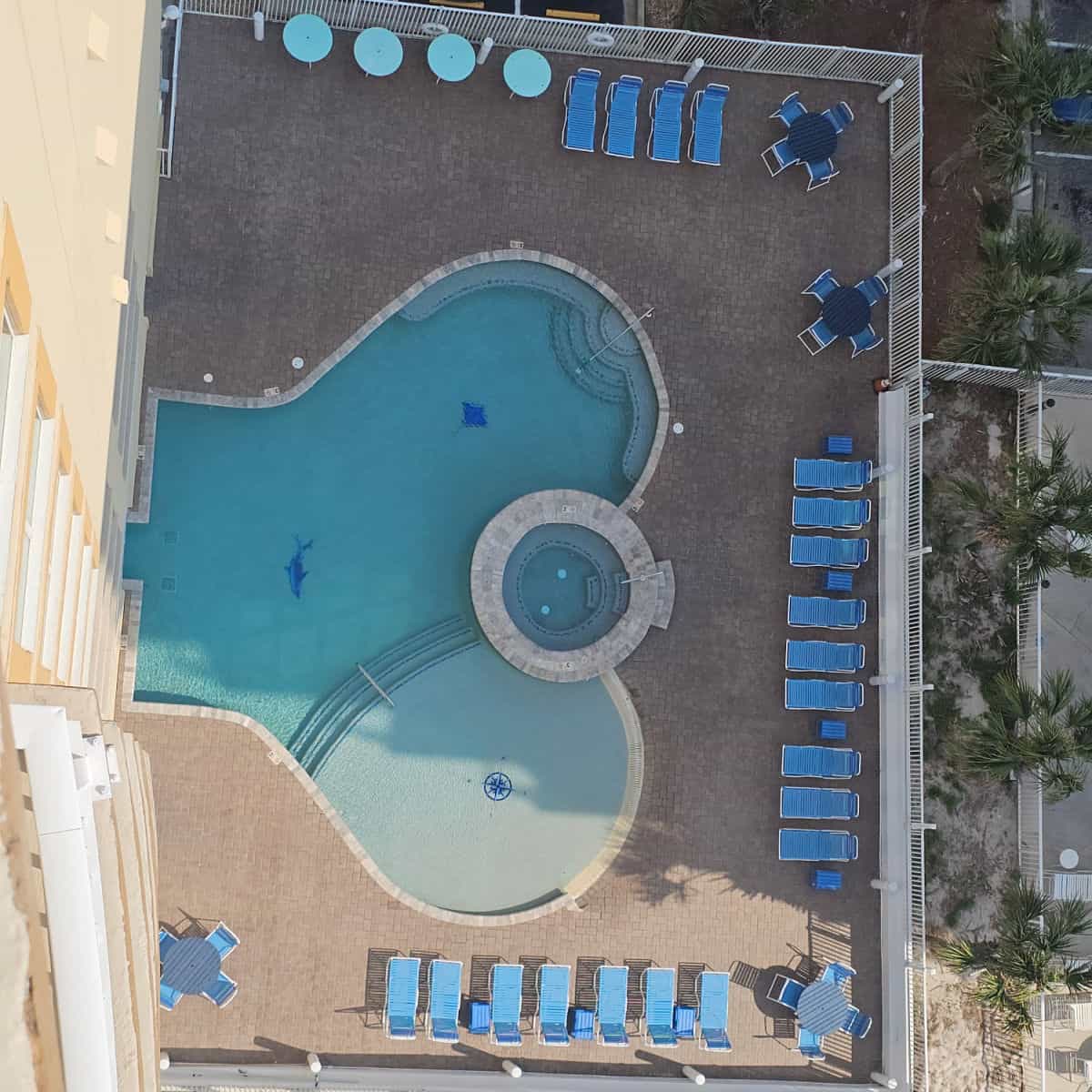 looking down on a pool with hot tub , bluechairs and tables on the pool deck, fence around the pool deck