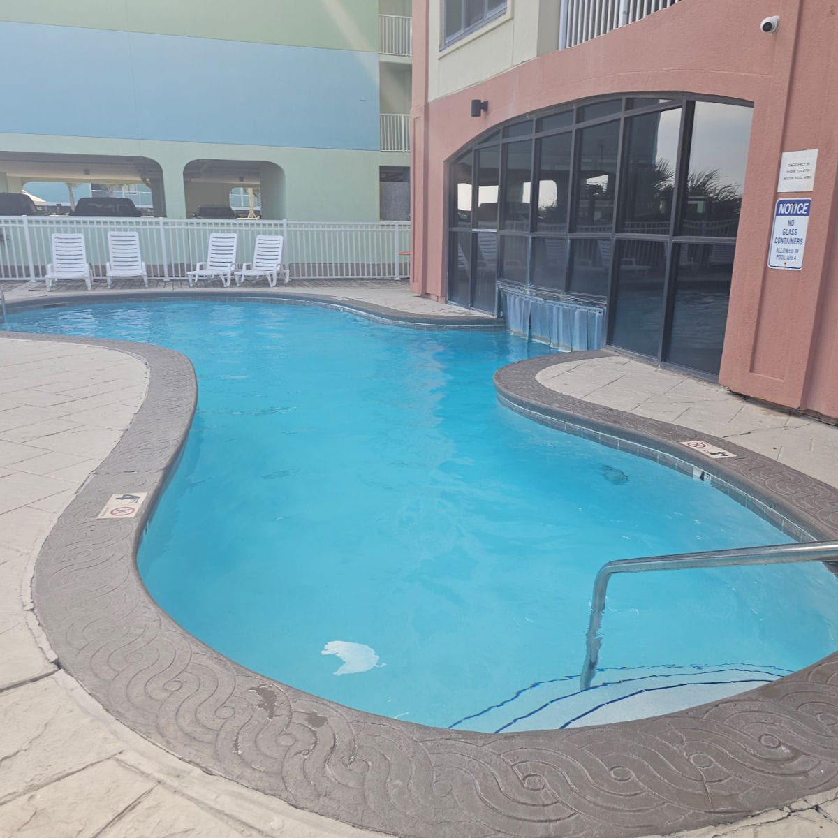 Curved outdoor pool with white lounge chairs, swim through area under windows on Harbour Place
