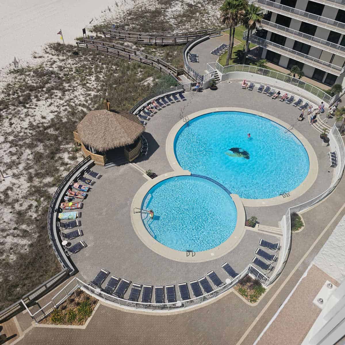 two outdoor pools with chairs around the edges, tiki hut in the middle, boardwalk down to the beach