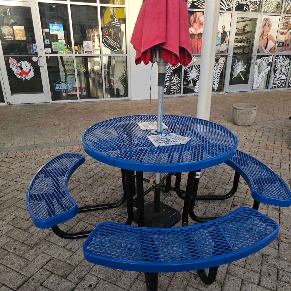 outside seating with a blue table with fixed benches, red umbrella not put up, next to the entrance to The Sugar Shack