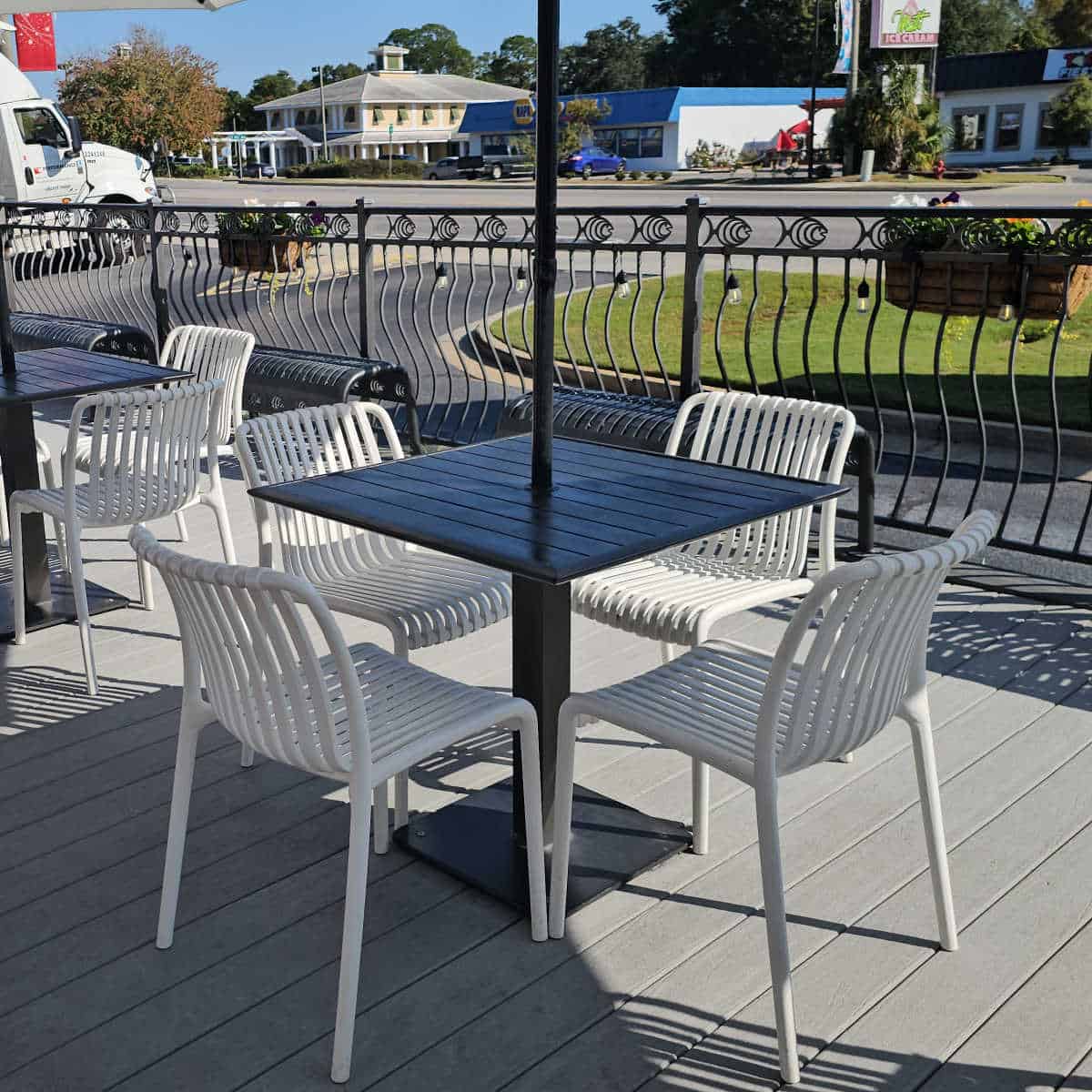 outdoor seating with white chairs and dark table, road in the background