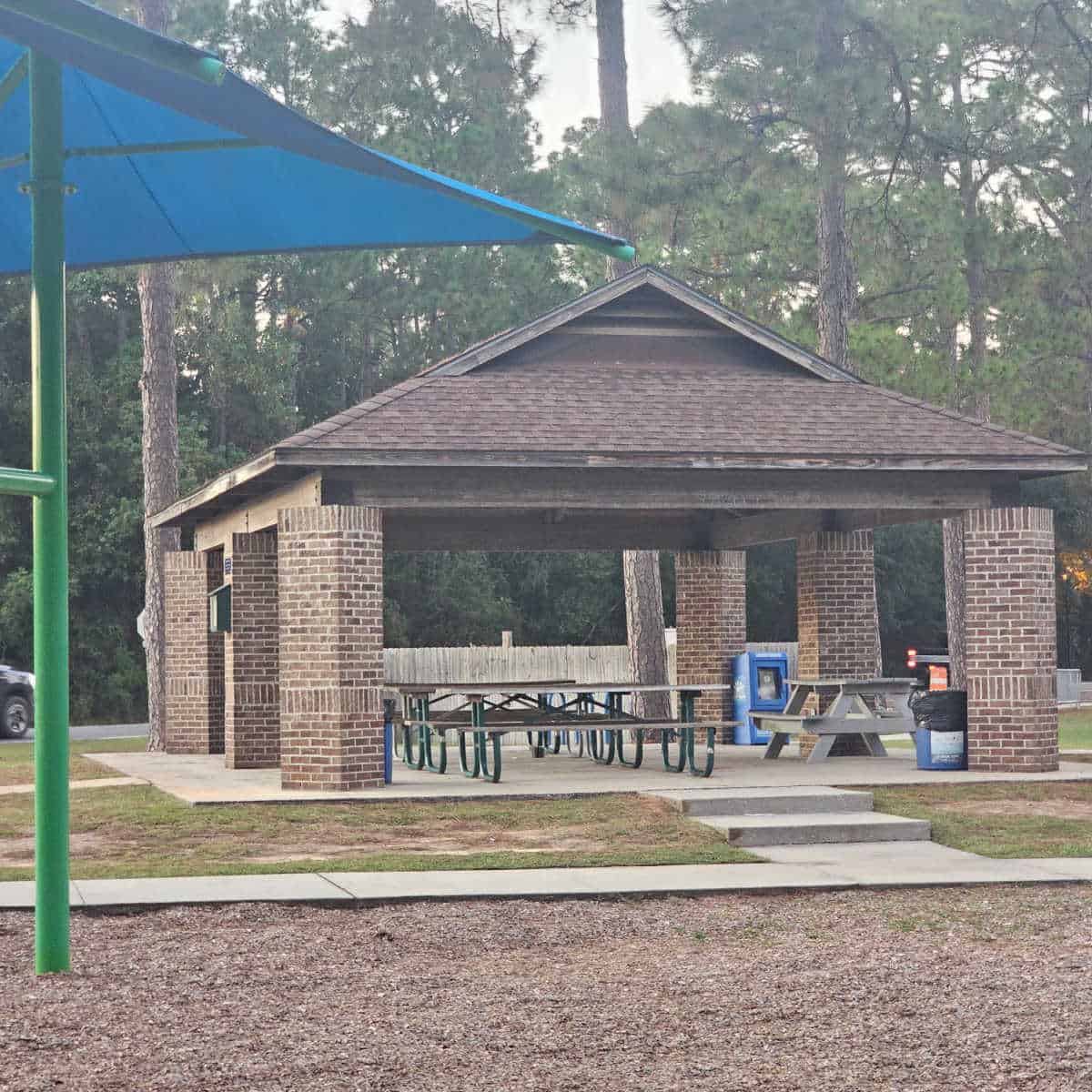 brick picnic shelter with picnic tables under it trees in the background.