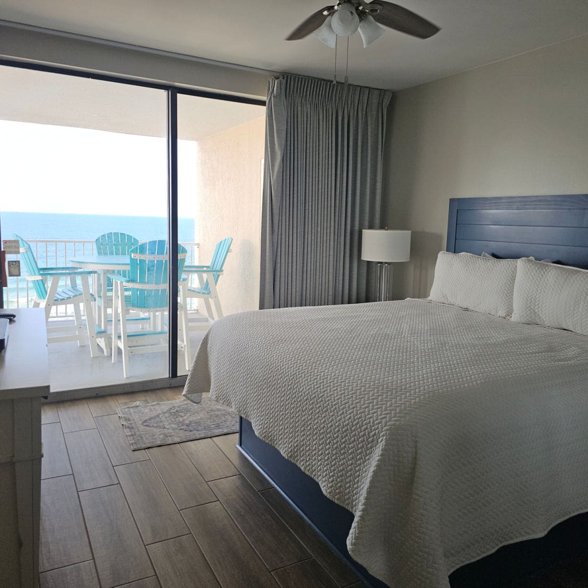 king size bed with blue backboard window looking to a table and chairs on the balcony with the Gulf in the background
