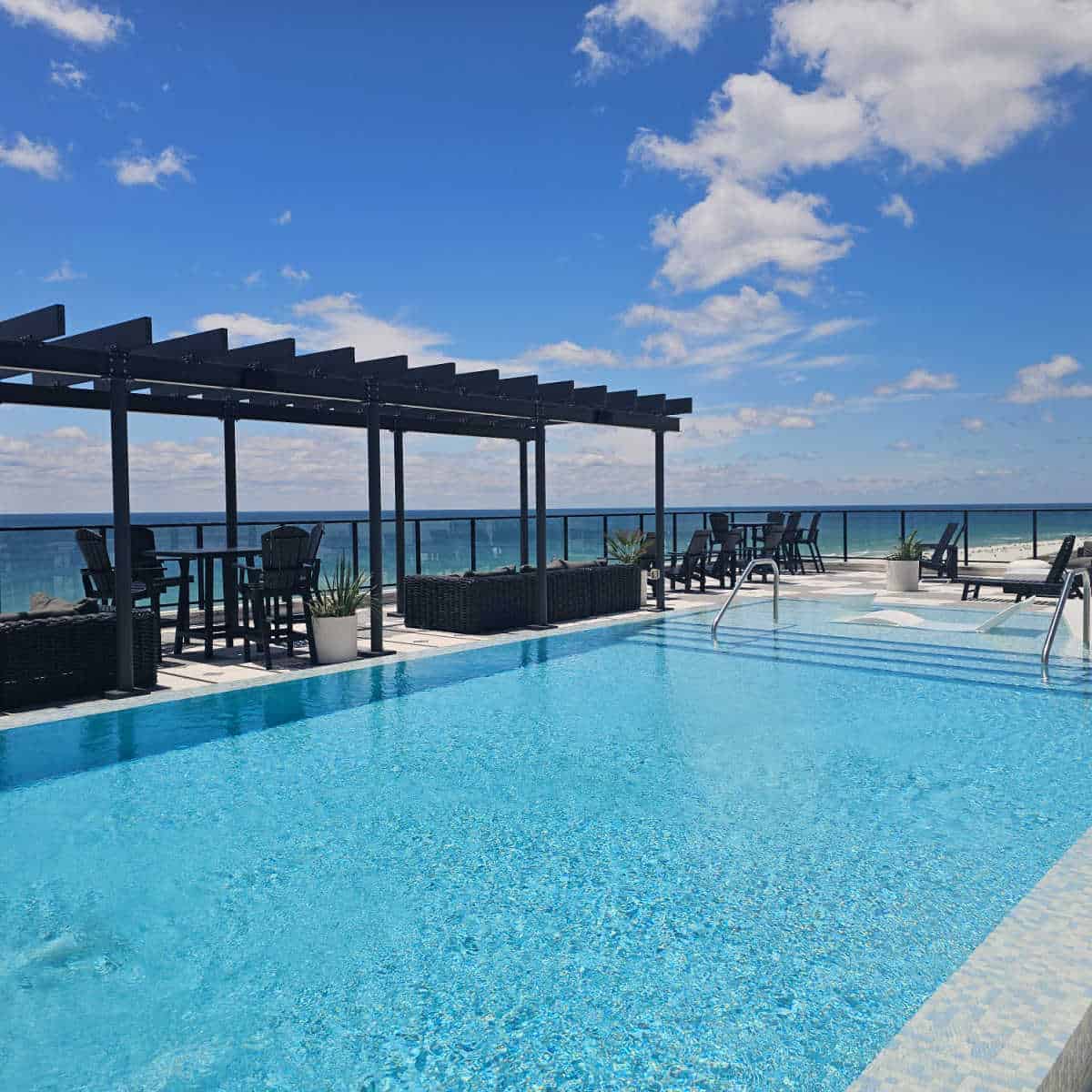 Rooftop pool with steps into the pool, chair in the shallow area, covered seating area overlooking the Gulf waters