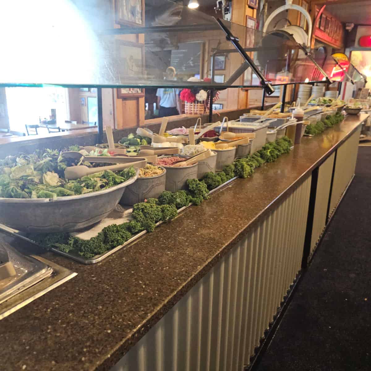 salad barwith items in containers and greenery along the edge
