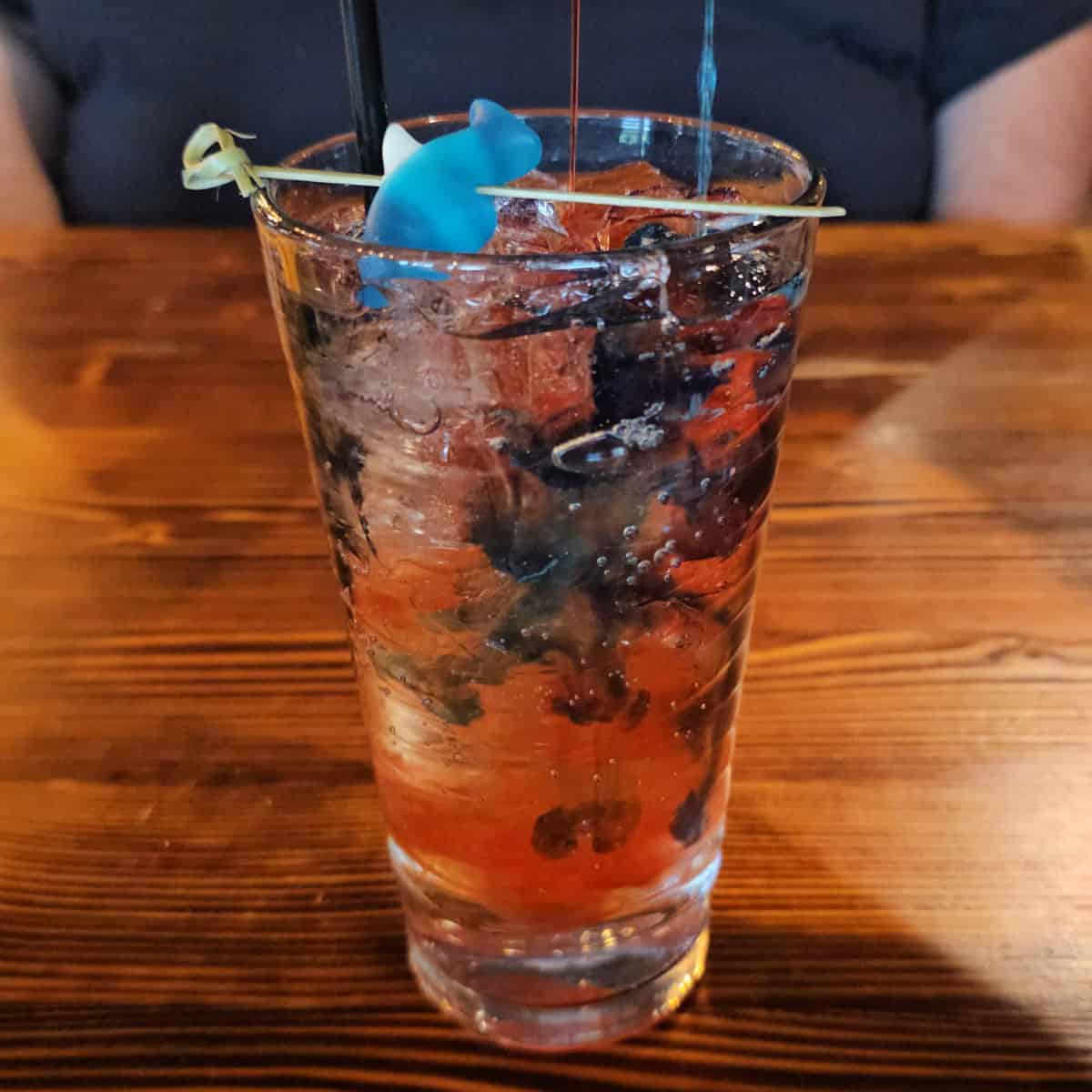 red and blue liquid pouring into a glass with a gummy shark in it