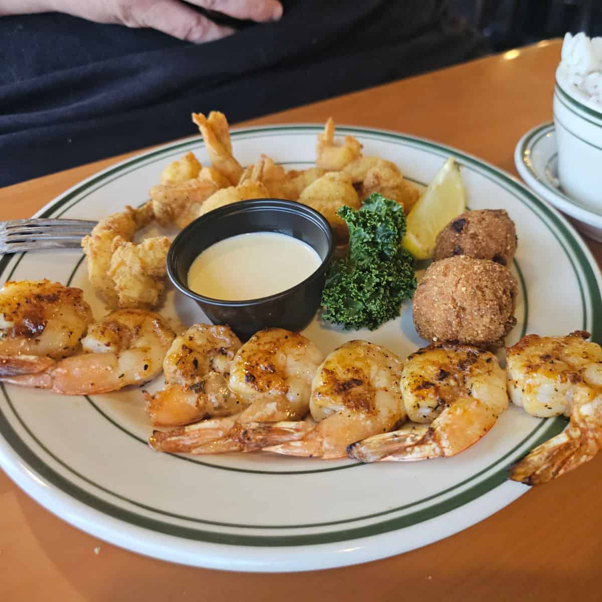 white plate with shrimp, hush puppies and sauce in a plastic container