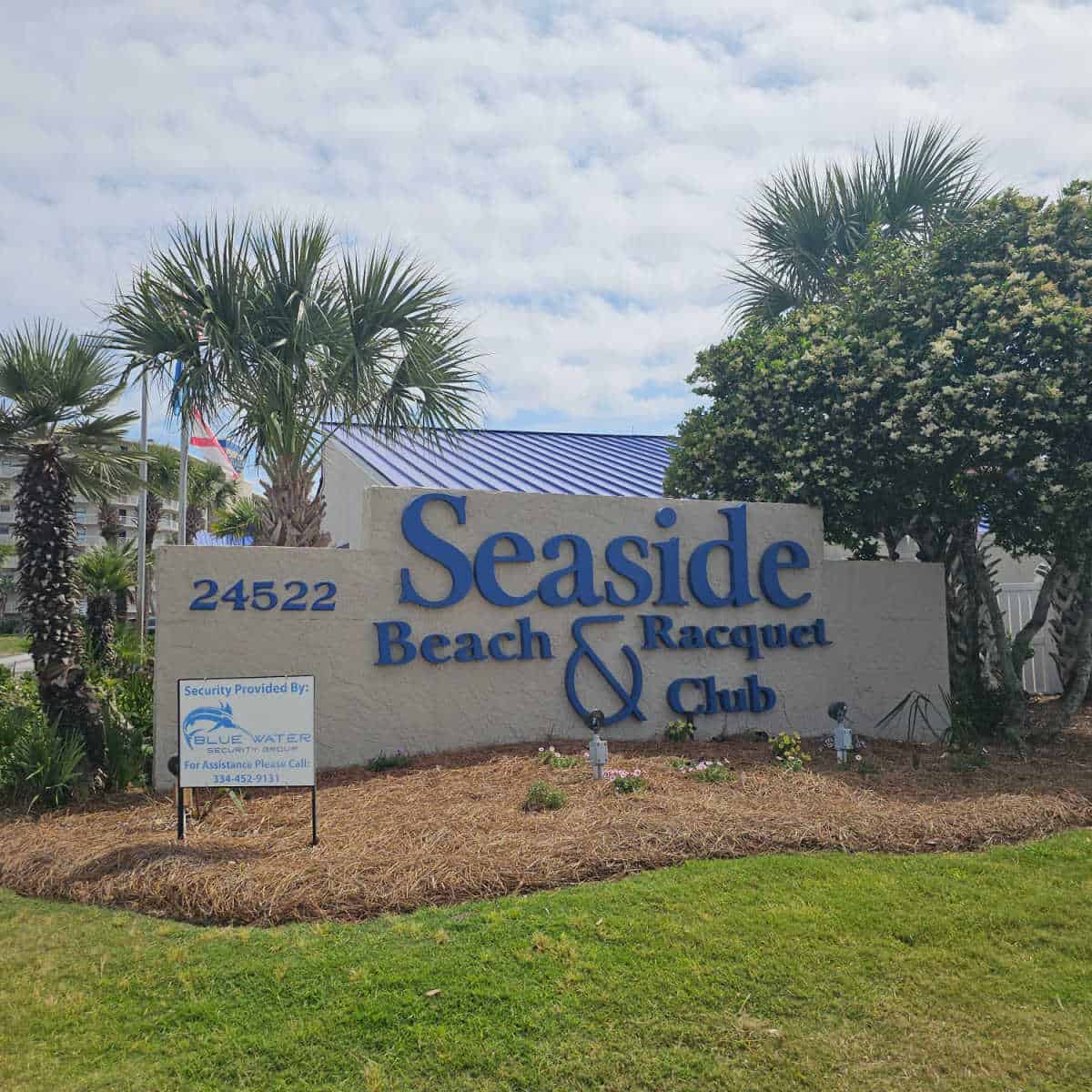 Seaside Beach & Racquet Club sign with trees and palm tree behind it
