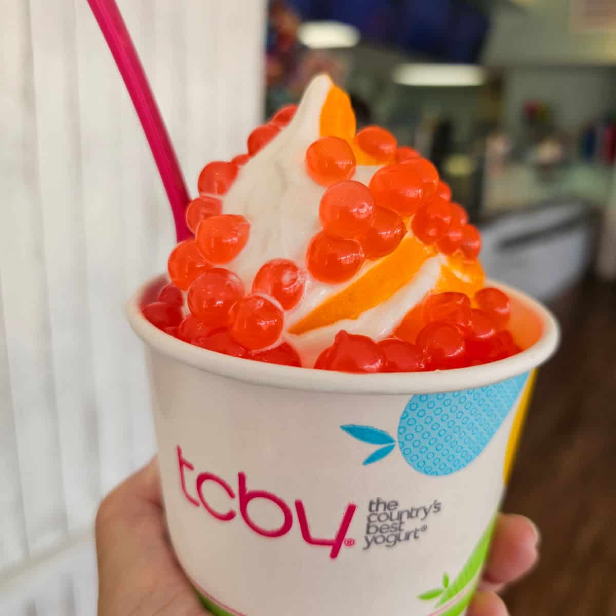 Hand holding a TCBY cup with frozen yogurt with boba pearls on it