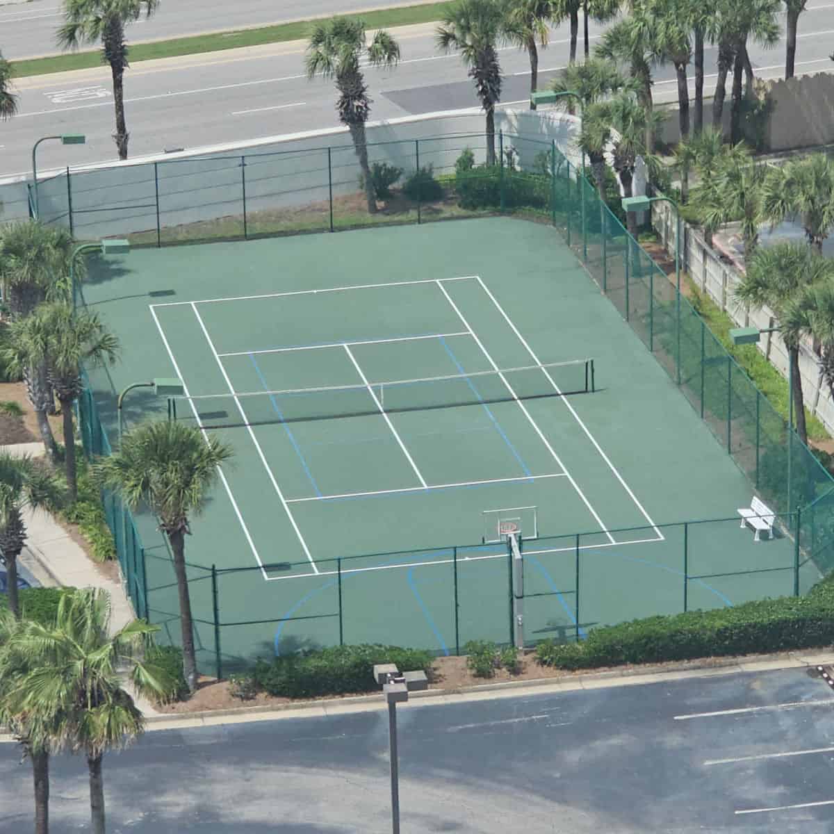 looking down over the tennis court with a basketball hoop at the end, road in the background