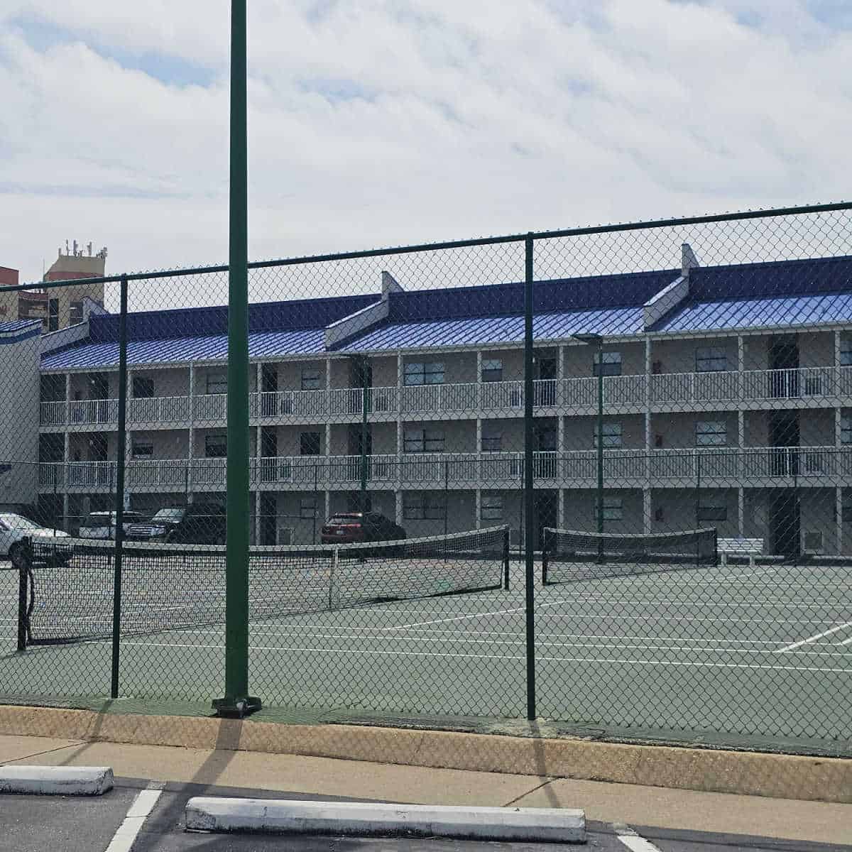 Tennis court behind a fence, with a blue roofed building behind the tennis court