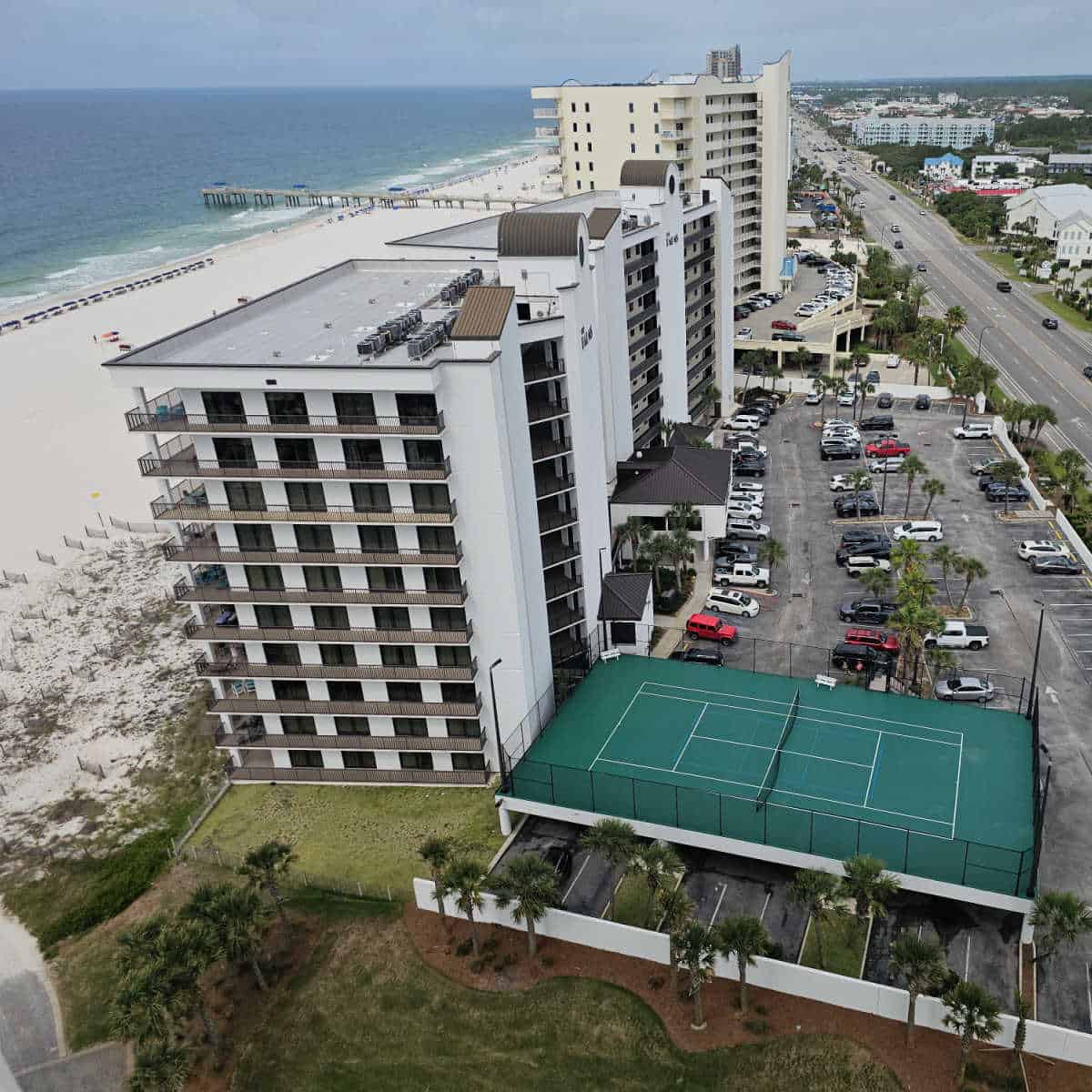 Looking over the Palms condo building with tennis court, parking lot, and beach access, Pier in the background