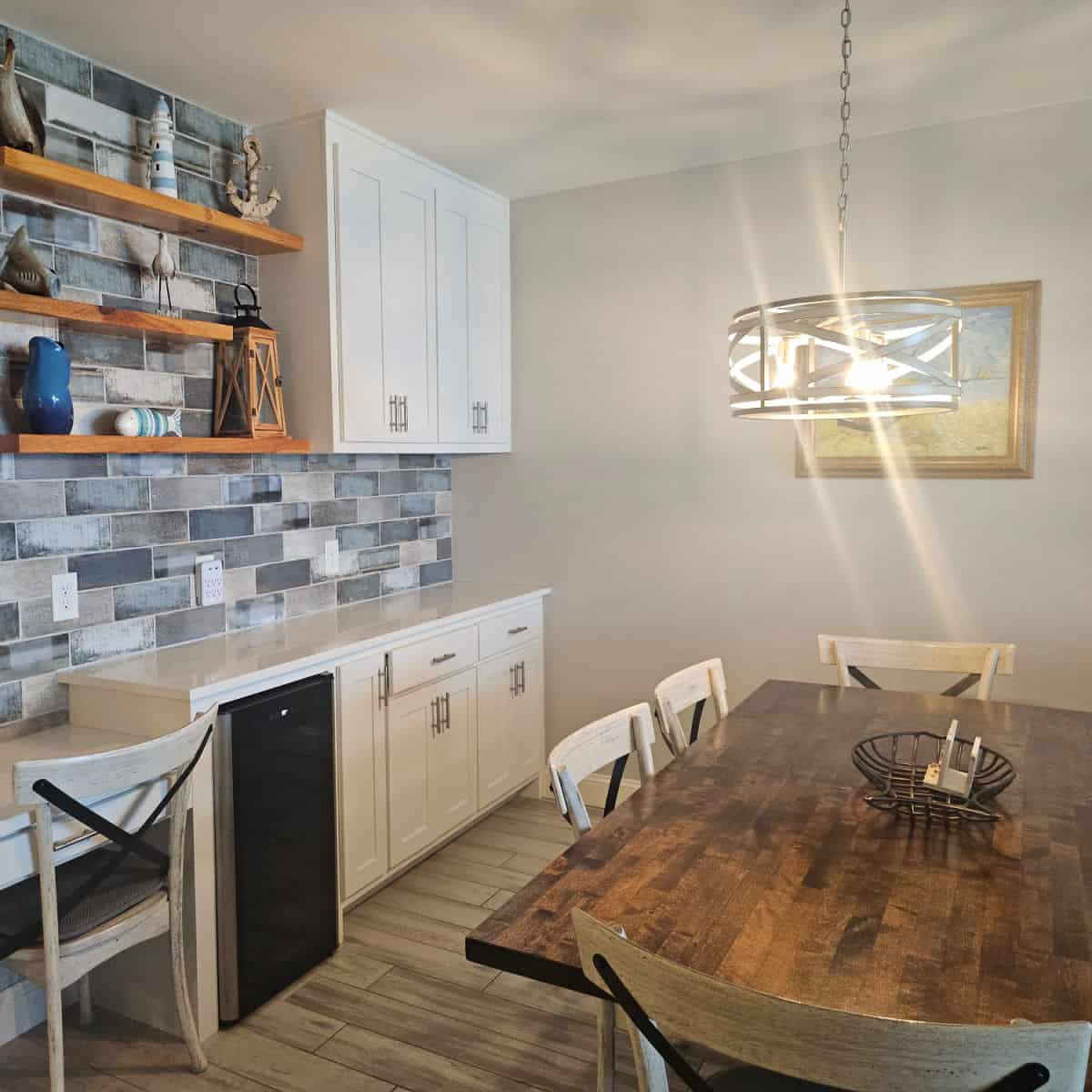 dining room table with chandelier over the top, cabinets on the wall with shelves filled with coastal items