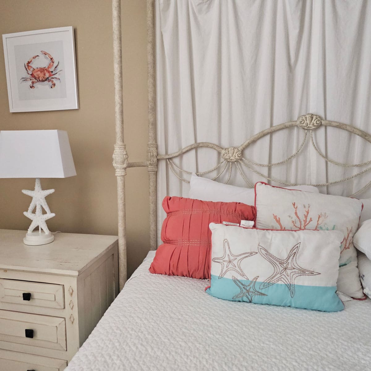 Bed with colorful coastal pillows, nightstand with starfish lamp, and an artistic image of a crab on the taupe walls