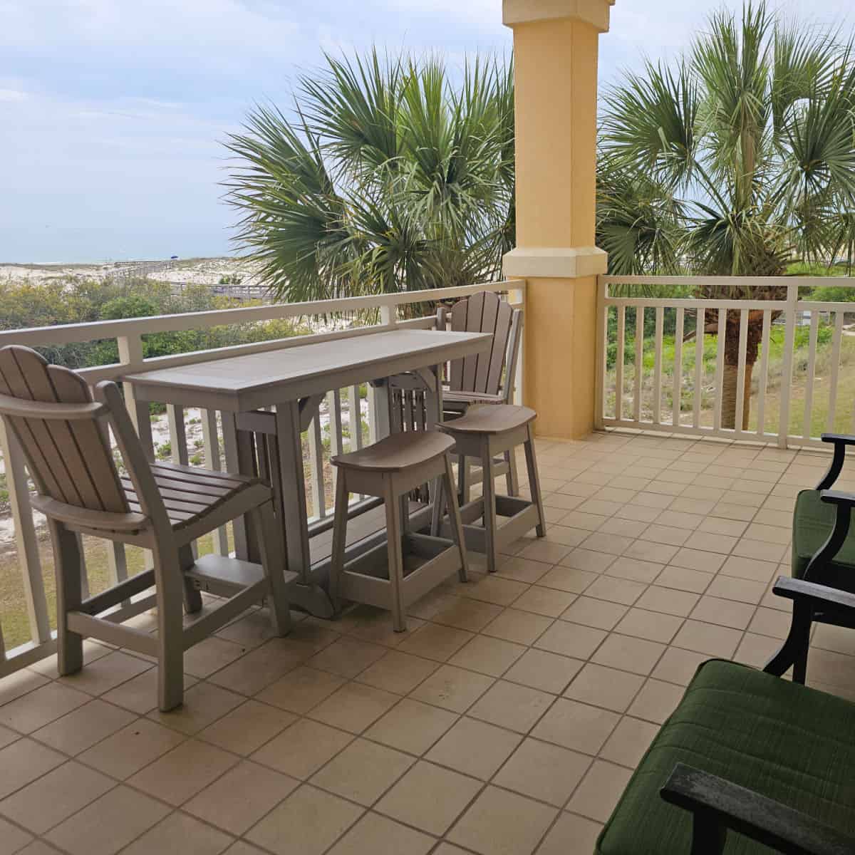 large balcony with green chairs, tables and chairs, sand dunes in the distance