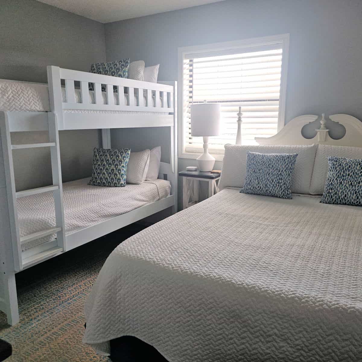bedroom with large queen bed and a bunkbed with white linens, nightstand with a white lamp