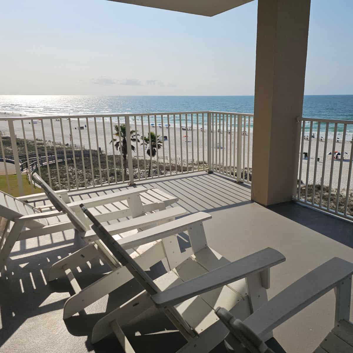 Balcony with white lounge chairs and Adirondack chairs with the Gulf in the background