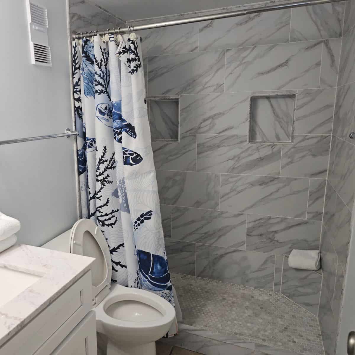 Bathroom with low entry step shower, marble tiles, white toilet, and part of the sink showing.