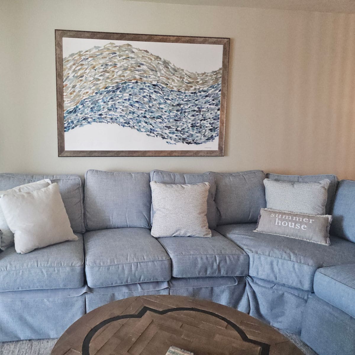 brown and blue art print on the wall, blue couch with pillows including summer house, wooden circle table