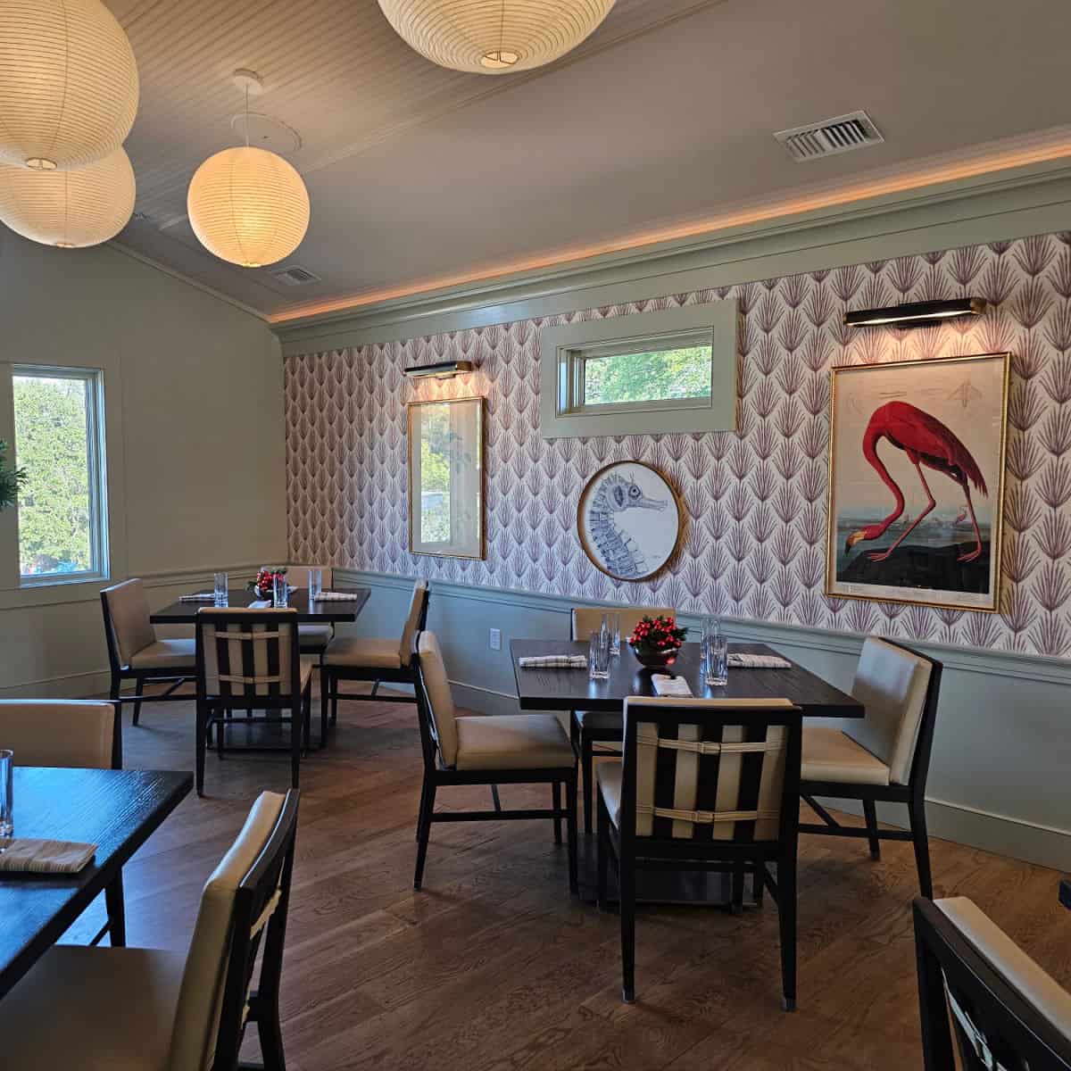 VIctory Hall with colorful wall paper covered with a flamingo print, seashore, and other art over tables and chairs