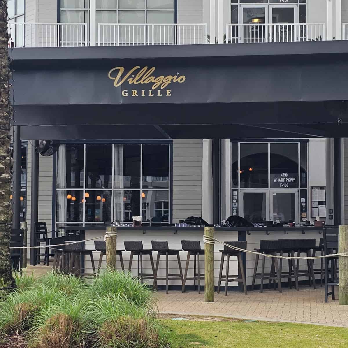 Villaggio Grille printed on the black awning over outdoor seating with tall chairs at a bar area
