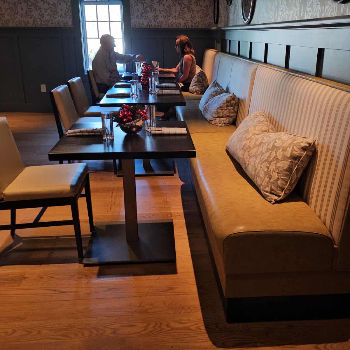 long padded bench with pillows along with a row of small tables and chairs against the bench
