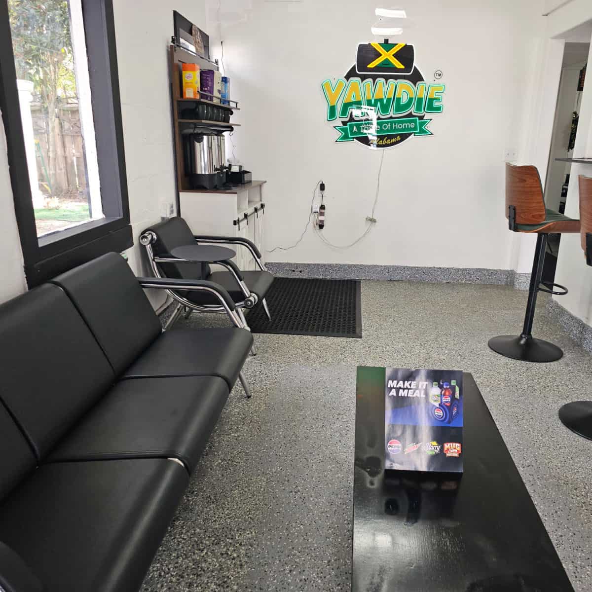 Yawdie neon sign on a white wall, black couch and chairs along the wall