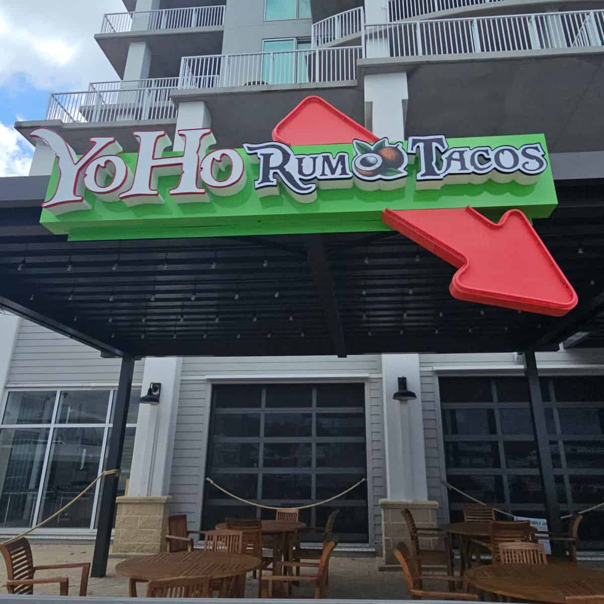 YoHo Rum & Tacos sign with a bright red arrow pointing down towards outdoor seating with tables and chairs