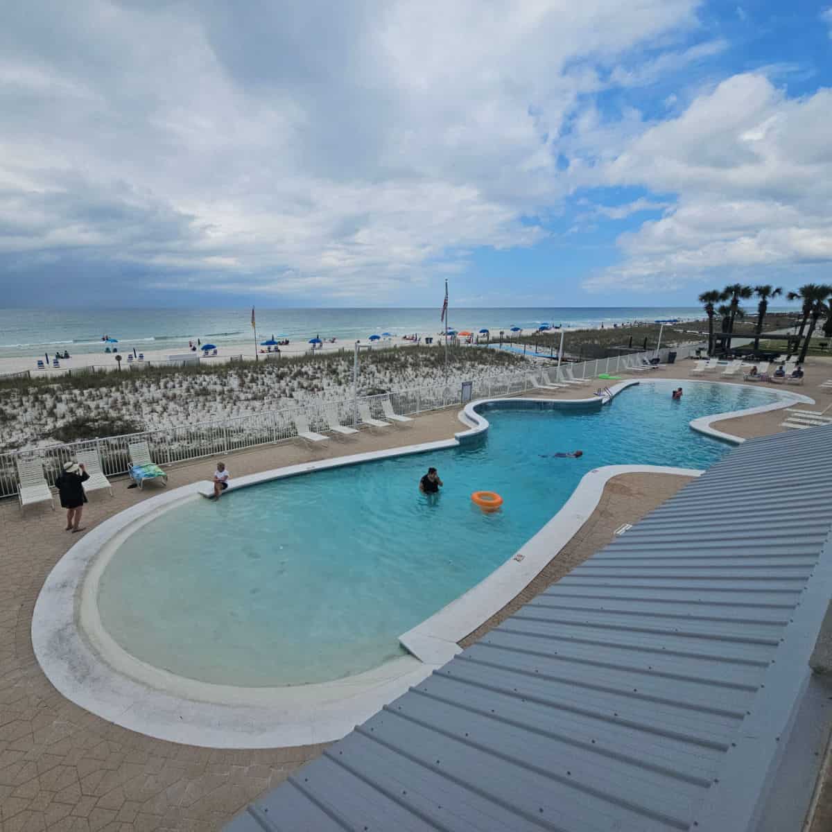 Looking down on the zero entry pool with people in the water, chairs around the pool deck, and the beach and Gulf in the background.