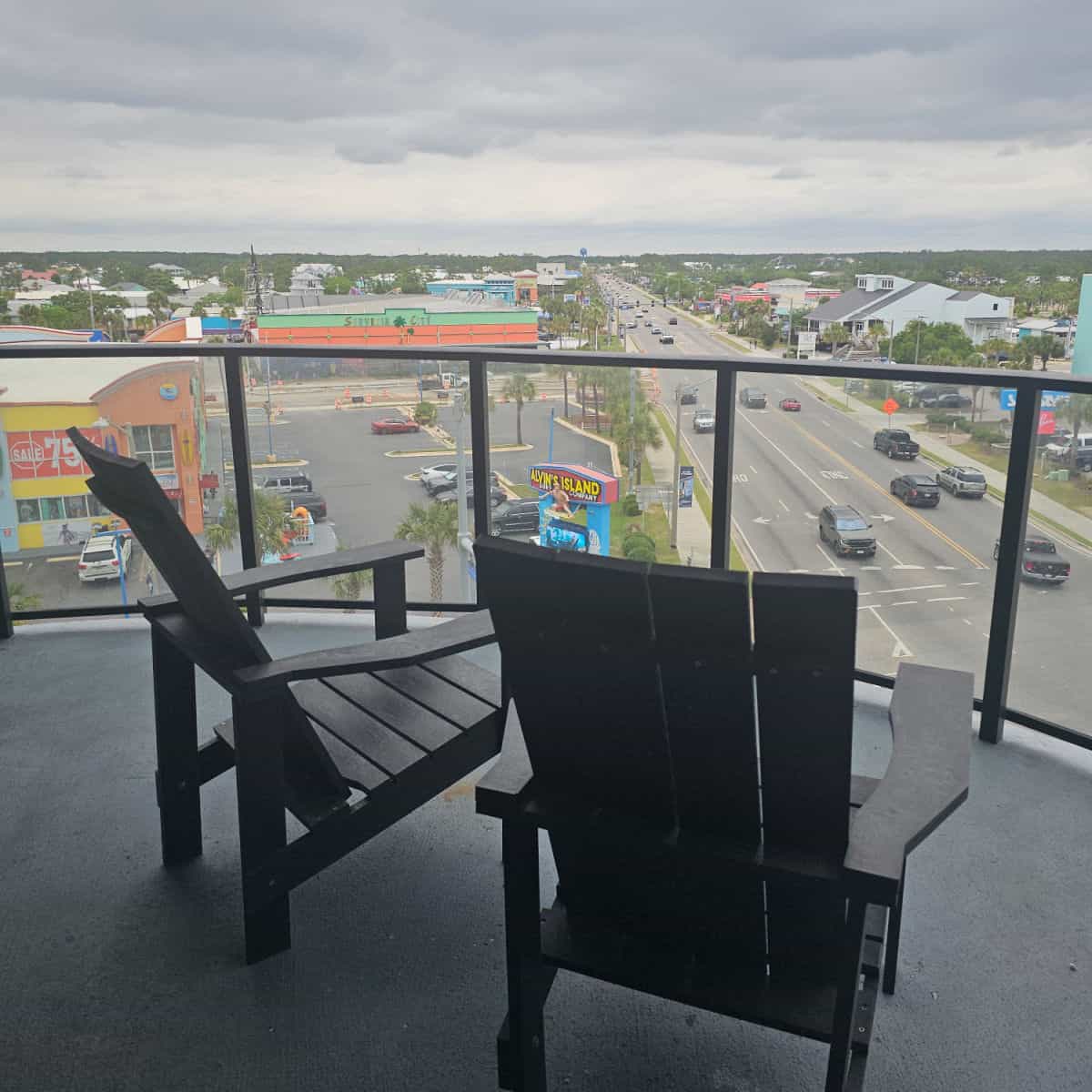 two Adirondack chairs on a balcony at Gulf Place Condos looking up hwy 59 past Alvins island, Souvenir City, cars in the road. Surf Style on the right