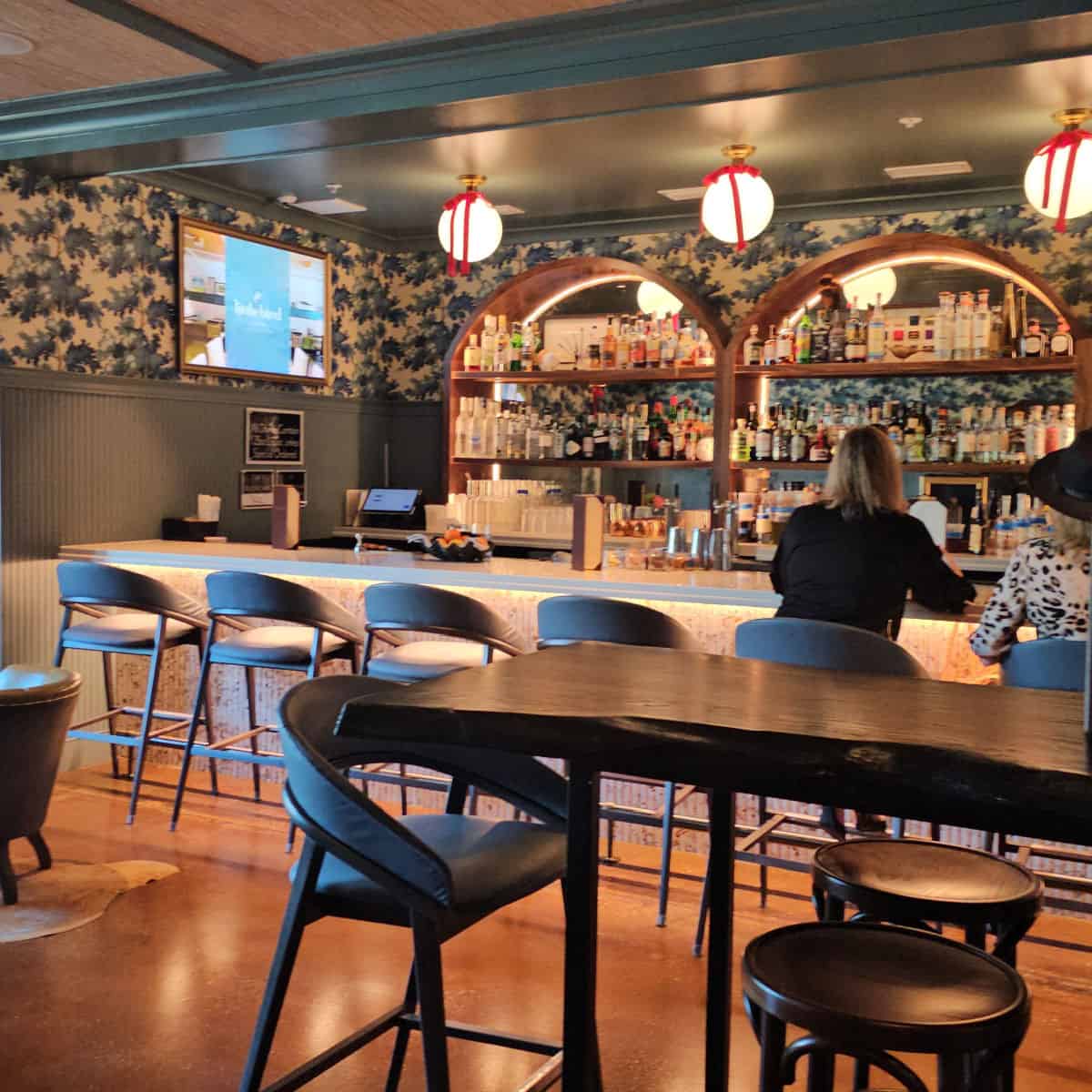 indoor bar area with people sitting at the bar in tall seats, white globe lights hanging over the bar