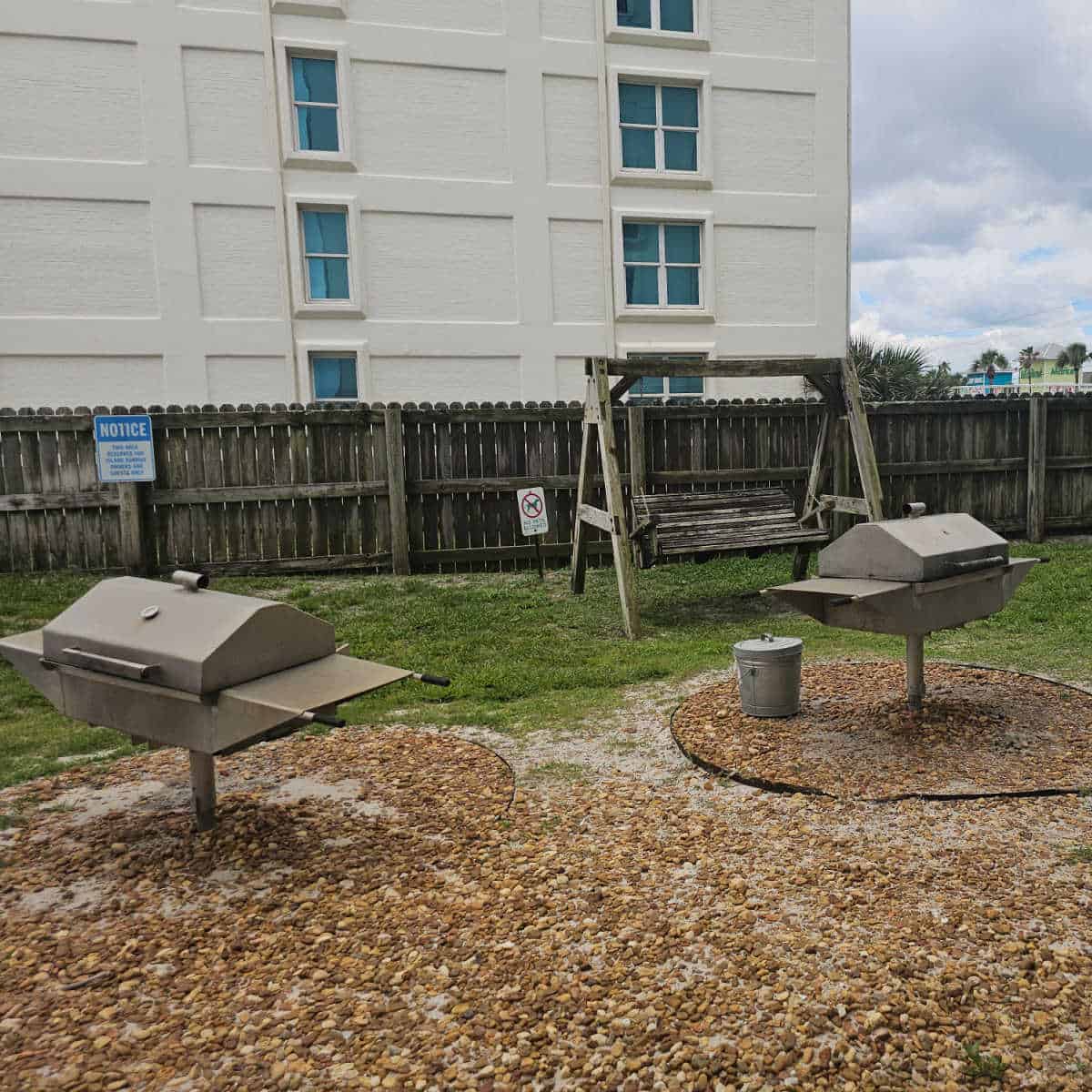 barbecues on a gravel area with a wooden swing in the background.