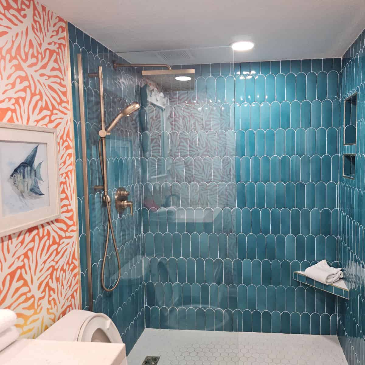 turquoise tiled shower with silver shower head next to an orange and white covered wall with fish art.