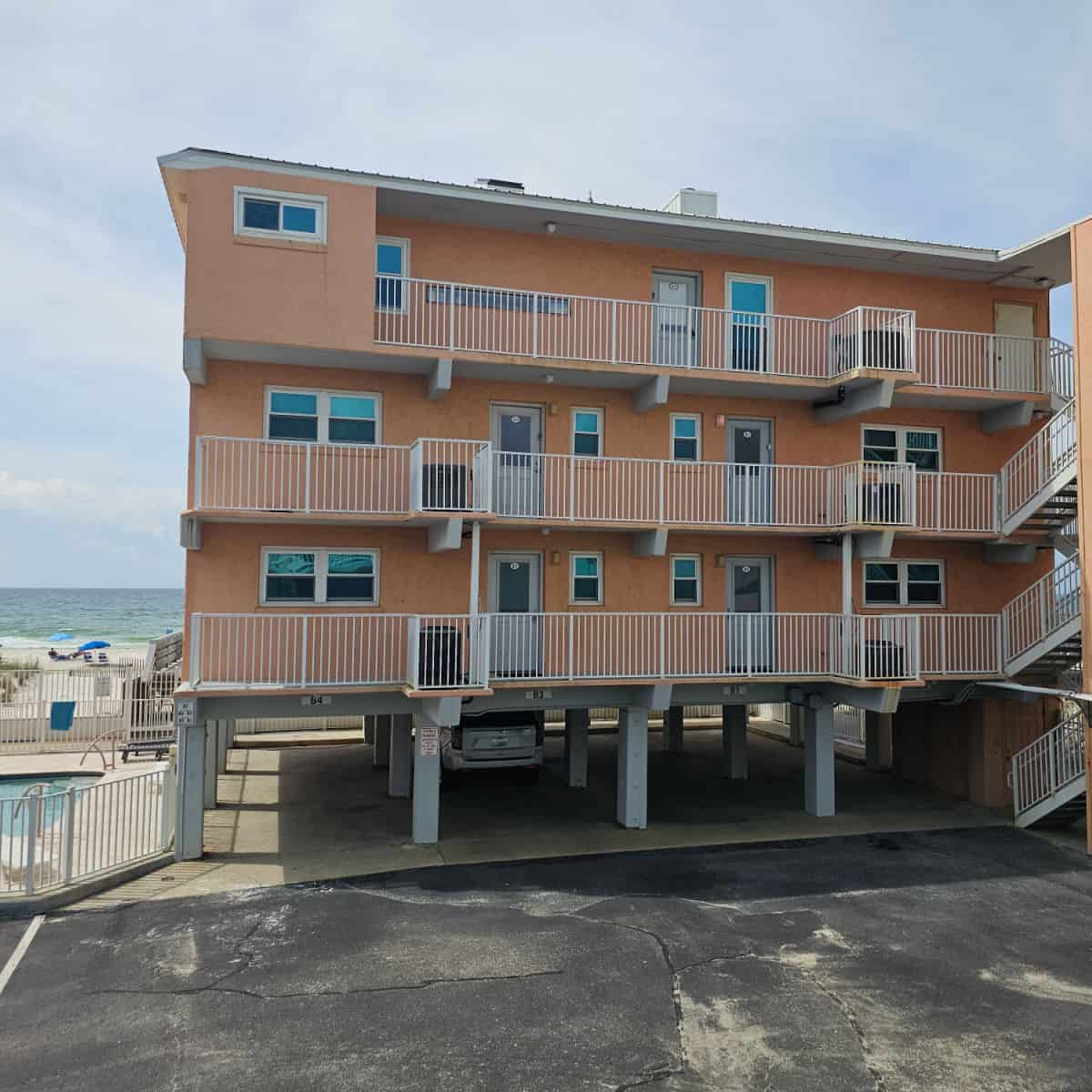 Tan colored 3 story building with stairs up the side, portion of the pool on the side